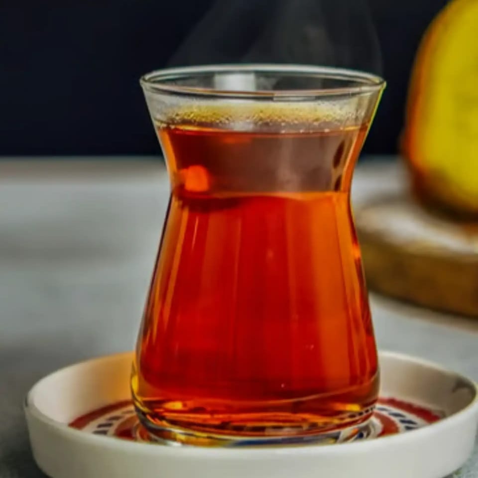 Steaming hot Turkish tea in a traditional tulip-shaped glass on a patterned saucer.