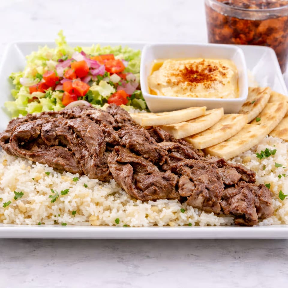 Shawarma plate with sliced meat, rice, salad, hummus, and pita bread on a white platter.