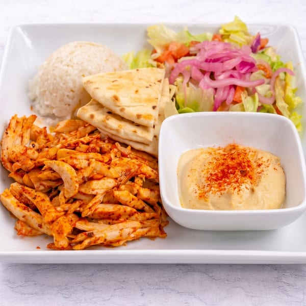 Chicken shawarma plate with rice, pita bread, salad with pickled onions, and hummus with paprika.